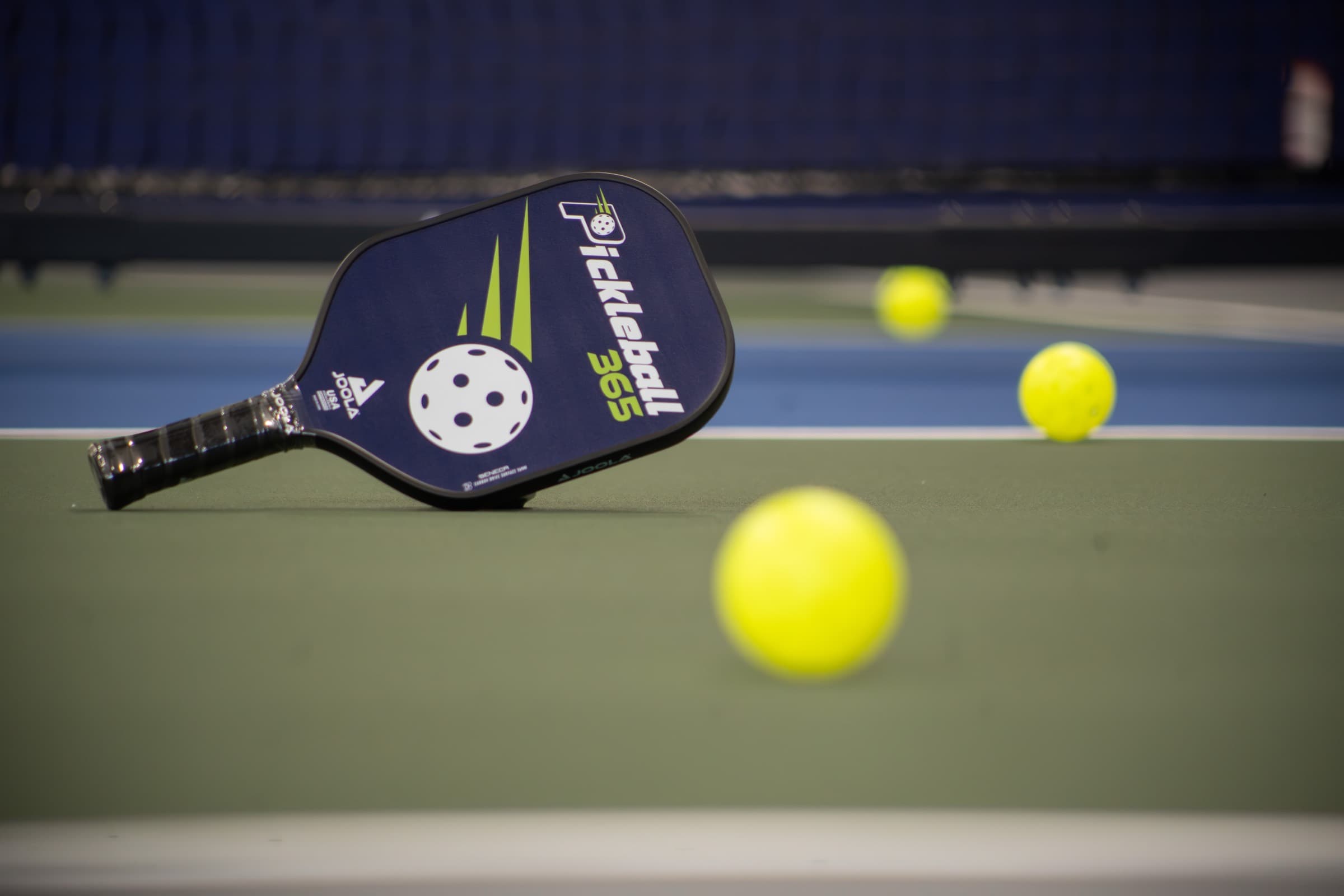 A Pickleball 365 branded paddle and balls on an indoor court